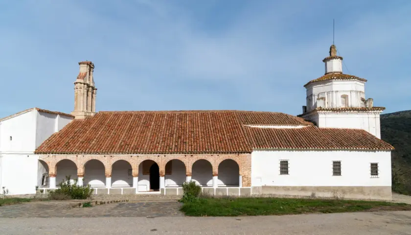 La ermita Virgen del Ara, con su tejado de tejas rojas y arcos blancos, se alza bajo un cielo azul.