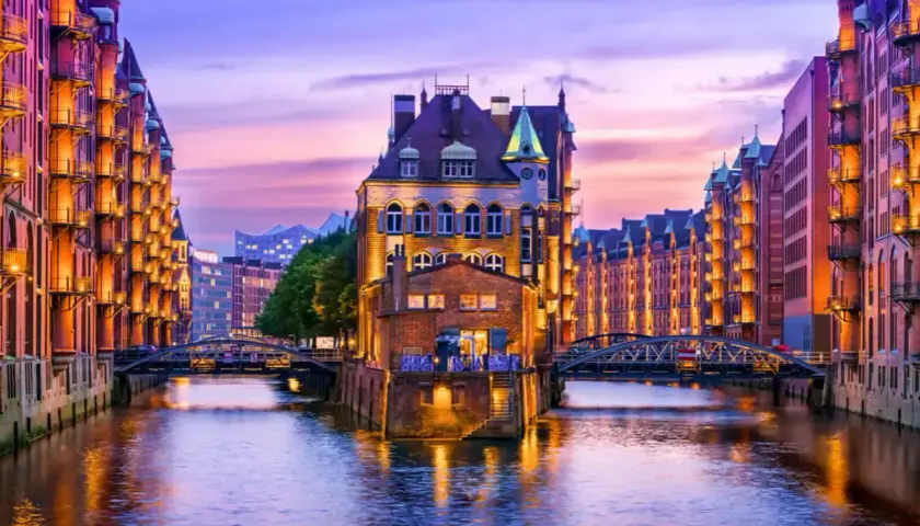 Canal de Hamburgo al atardecer, perfecto para saber donde ir en el puente de diciembre. Edificios de ladrillo iluminados reflejándose en el agua.