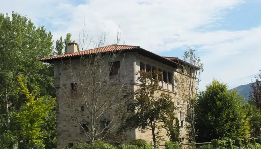 Edificio de piedra con tejado rojo y balcones, rodeado de árboles verdes. Un lugar con encanto, ideal para saber artziniega como llegar.