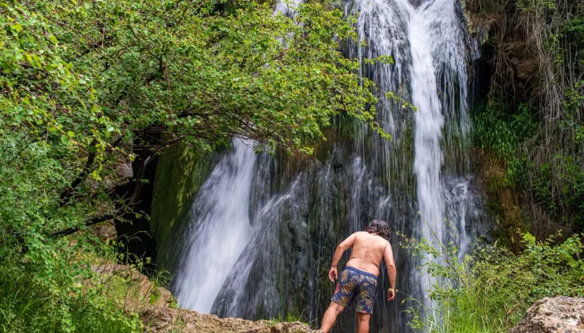 Hombre de espaldas admira la cascada en la ruta del barranco de la Hoz. Naturaleza exuberante y agua en movimiento.