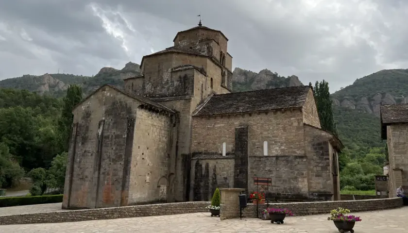 Iglesia románica de piedra con montañas al fondo. Un lugar histórico que evoca la grandeza del puente la reina.