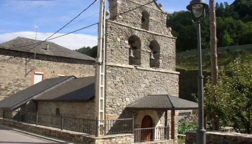 Iglesia de piedra en La Portela de Valcarce, con campanario de dos arcos y campanas. Un farol ilumina la entrada.