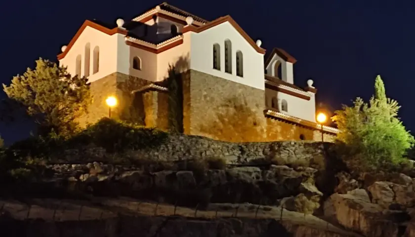 La ermita de los Tres Juanes, iluminada de noche, se alza sobre una colina rocosa.