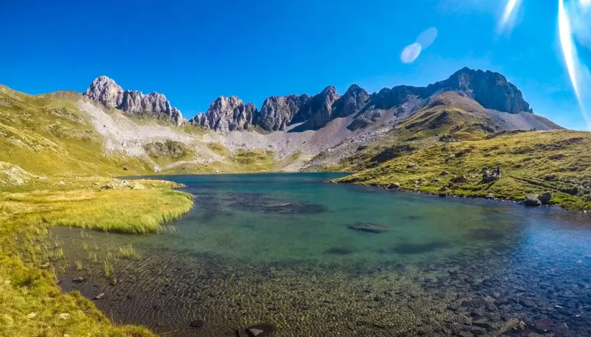El ibón de Acherito, un lago de montaña de aguas cristalinas, rodeado de prados verdes y picos rocosos bajo un cielo azul intenso.