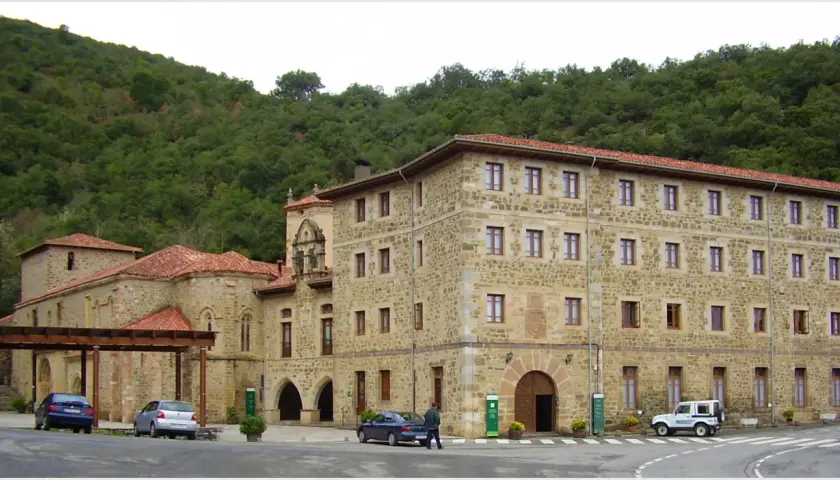 Edificio de piedra con tejados rojos, parte del monasterio de Santo Toribio de Liébana, rodeado de vegetación.