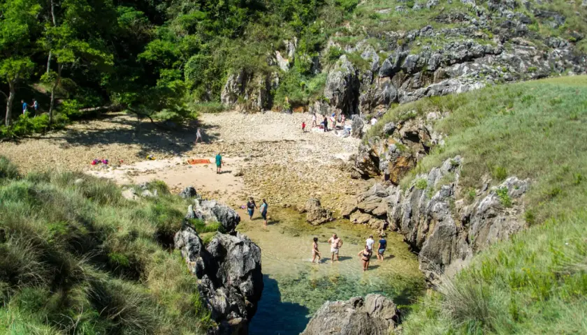 Gente disfrutando del sol y el agua cristalina en la playa de cobijero, rodeada de rocas y vegetación exuberante.