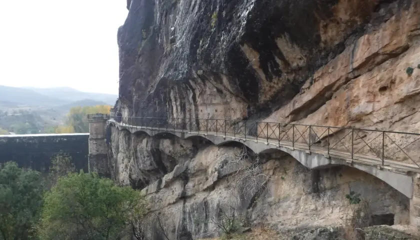 Un pontón de la oliva se aferra a un acantilado rocoso, con un camino bordeado de barandillas que serpentea a lo largo.