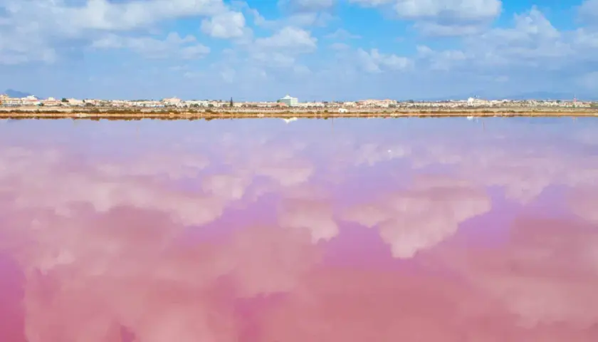 El agua rosa de la playa de Murcia refleja las nubes blancas bajo un cielo azul. Un paisaje surrealista y hermoso.