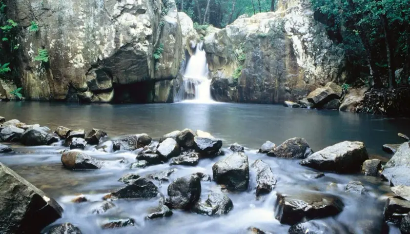 Cascada y río en la ruta del Río de la Miel, rodeado de rocas y vegetación exuberante.