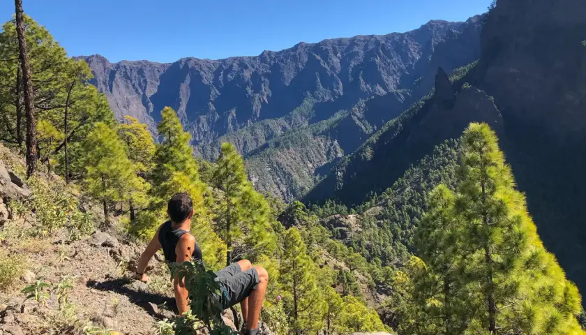 Hombre sentado en la ladera, contemplando el imponente paisaje montañoso del **cubo de la galga**.