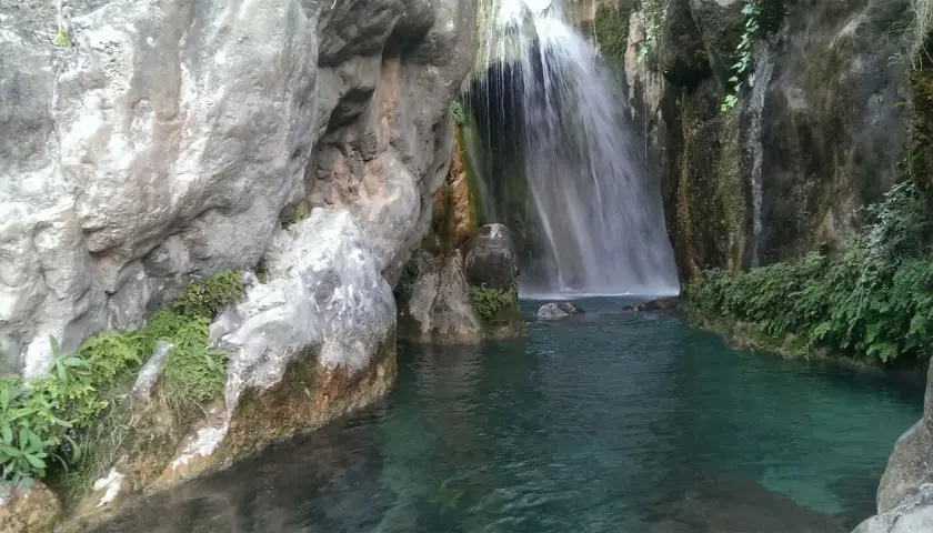 Cascada en las fuentes del Algar, con aguas turquesas y vegetación exuberante entre rocas.