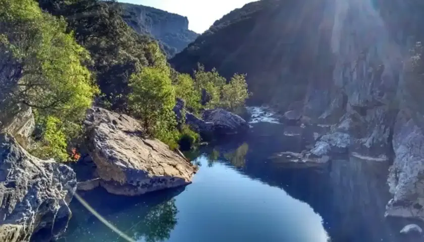 Río sereno en la Foz de Lumbier, un paisaje ideal para una ruta. Rocas y vegetación bordean el agua azul bajo el sol.