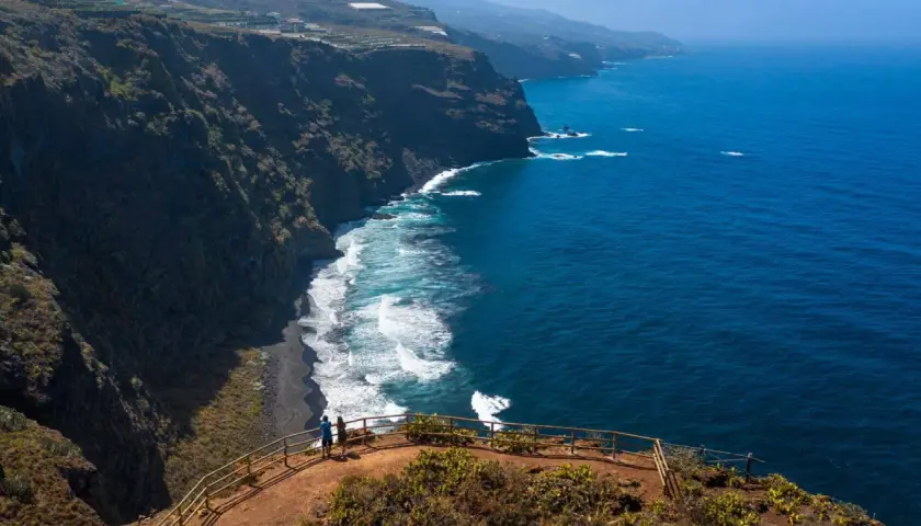 Pareja admira la playa de nogales, una costa volcánica de arena negra bañada por el azul intenso del océano.