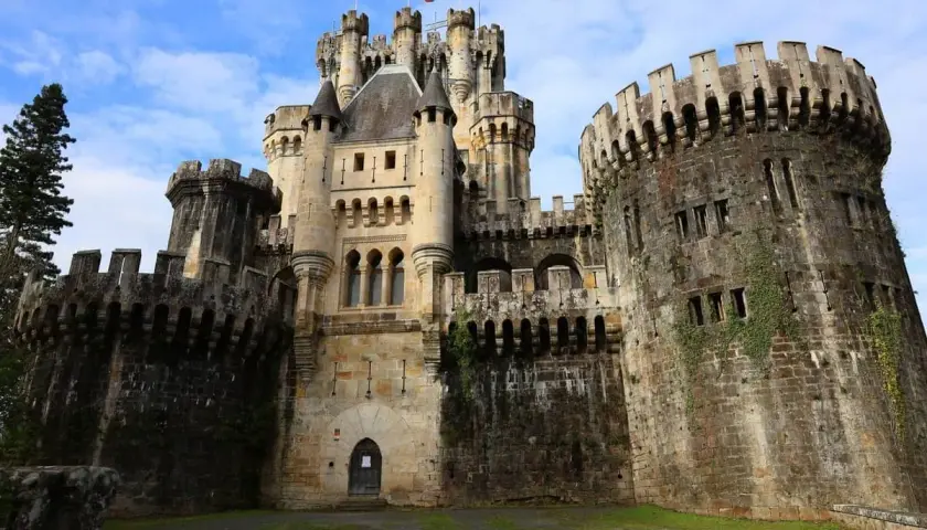 El imponente castillo de Butrón, con sus torres y murallas de piedra, se alza majestuoso bajo un cielo azul con nubes.
