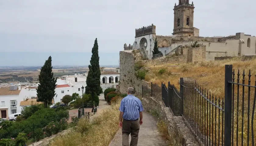 Hombre camina por sendero hacia iglesia en Medina Sidonia. Descubre cómo llegar a este pueblo blanco andaluz.
