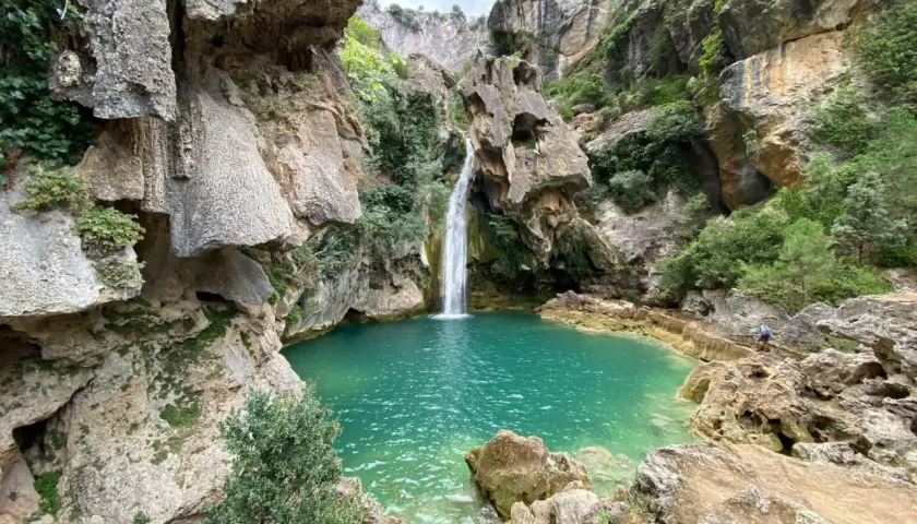 La cascada de la calavera cae en una poza de agua turquesa, rodeada de rocas y vegetación exuberante.