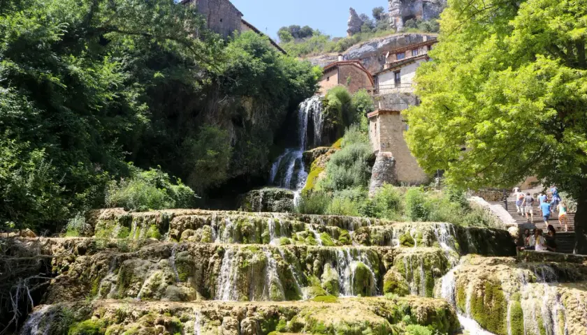 Cascada en las Hoces del Ebro, con casas de piedra integradas en la roca y vegetación exuberante.