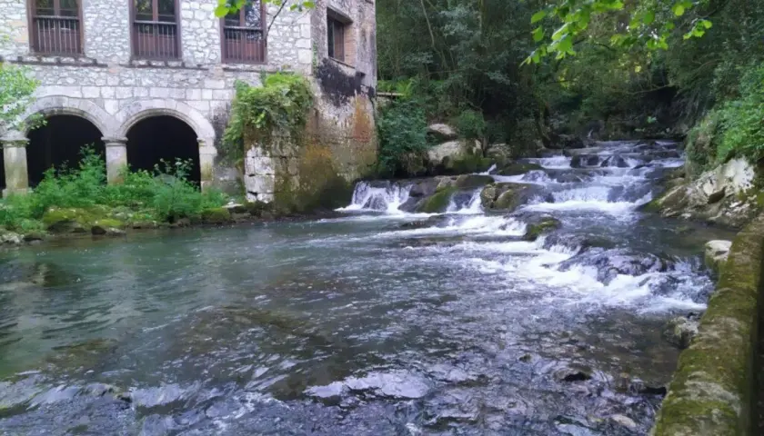 Edificio de piedra con arcos junto a un río con cascadas. Parece la fuente del francés, un lugar idílico.