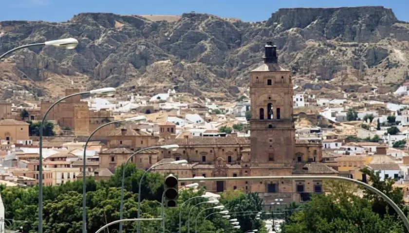Vista panorámica de Guadix, con su imponente torre campanario y casas blancas al pie de montañas rocosas. Ideal para planificar cómo llegar.