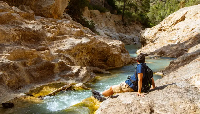 Hombre sentado junto a un río turquesa en un cañón rocoso. Un lugar idílico para explorar, ¡así es como llegar!