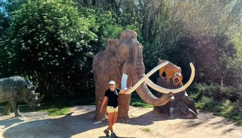 Una mujer sonríe junto a un mamut y un tigre dientes de sable, parte de la ruta del mamut. Un rinoceronte se ve a la izquierda.