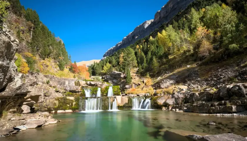 Cascada en un valle montañoso con árboles otoñales, ideal para las mejores rutas senderismo España.
