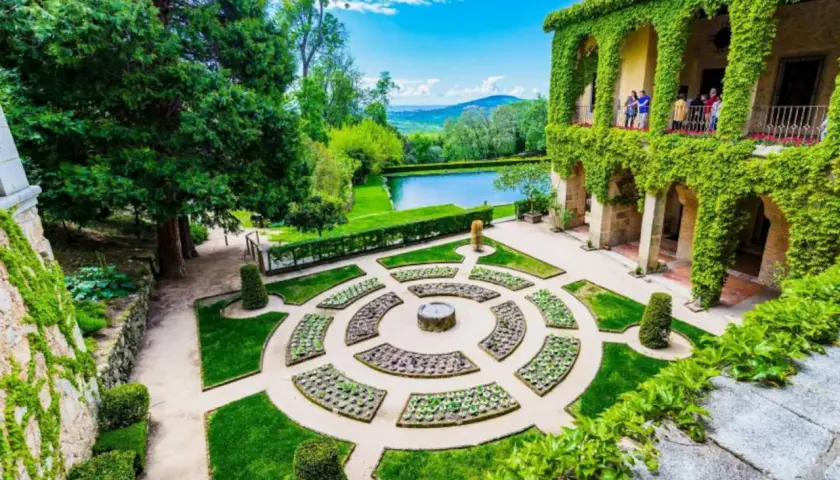 Jardín renacentista con estanque y edificio cubierto de hiedra, evocando la serenidad de los Cuacos de Yuste.