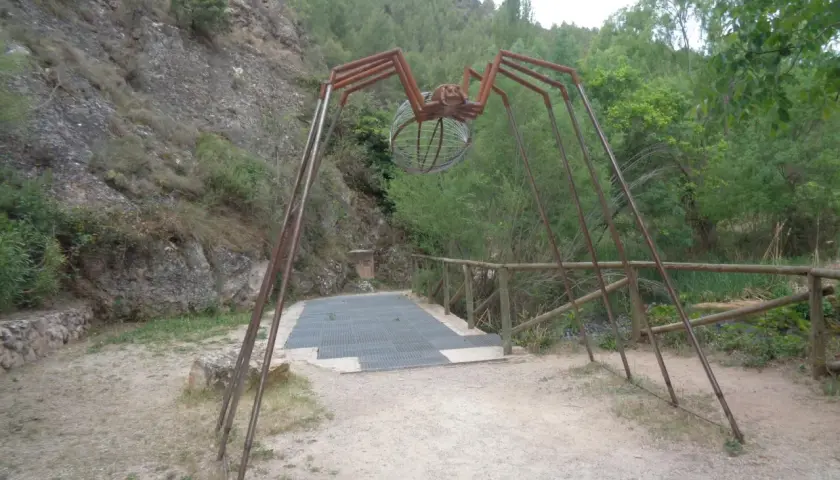 Escultura de araña gigante en la ruta de las esculturas Bogarra, con un cuerpo de alambre y patas metálicas, sobre un camino de grava.