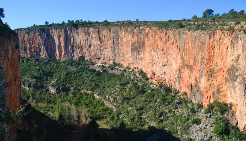 Impresionante cañón con paredes rojizas y vegetación verde. Los puentes colgantes de Chulilla se asoman entre la naturaleza.