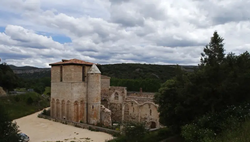 Ruinas del monasterio de San Pedro de Arlanza, con su torre robusta y arcos de piedra bajo un cielo nublado.