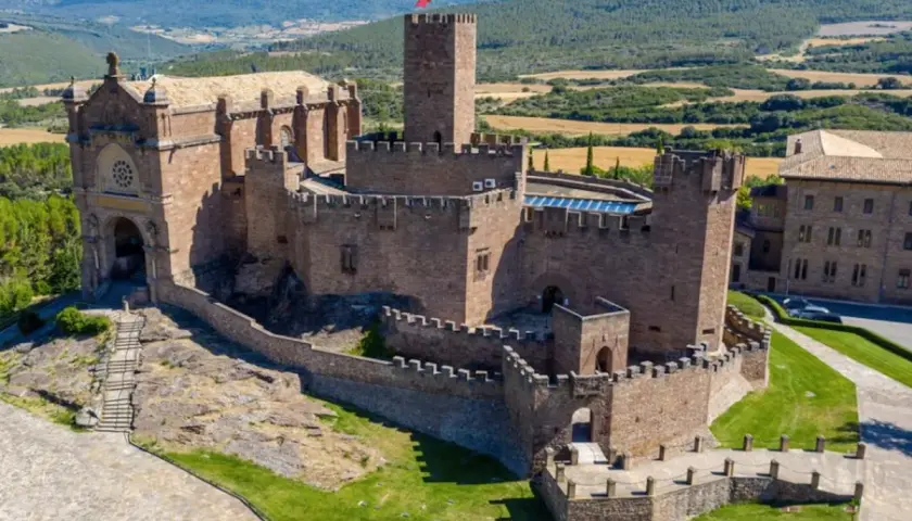 Imponente castillo de Javier, con su basílica anexa y torres defensivas, se alza majestuoso sobre un paisaje verde y montañoso.