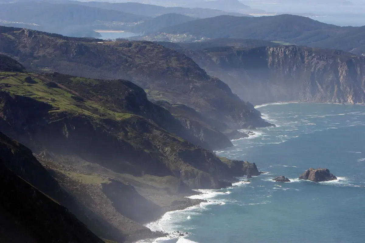 Majestuosos acantilados de San Andrés de Teixido se alzan sobre el mar Cantábrico, con verdes laderas y el azul profundo del océano.