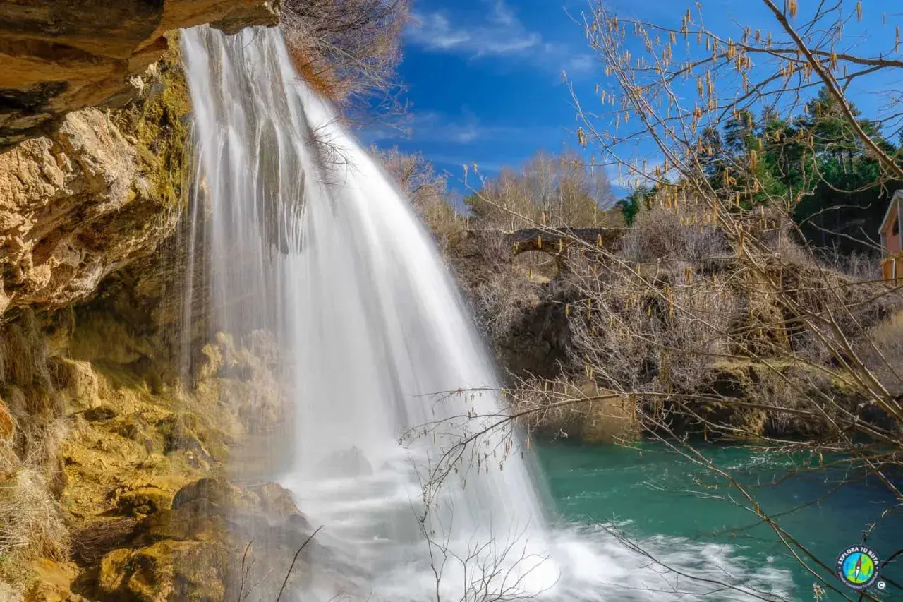 Cascada de agua blanca cayendo sobre rocas ocres, como los ojos del Cabriel, en un día azul.