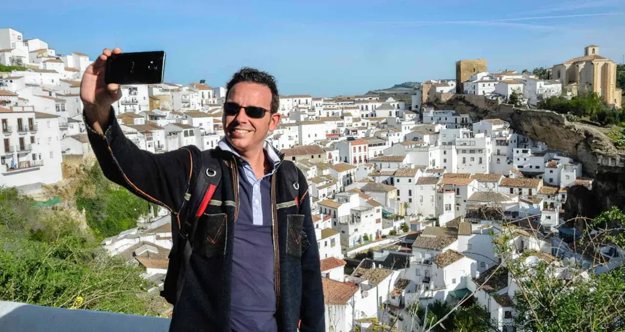 Hombre sonriente se toma selfie con el pueblo blanco de Bornos al fondo. ¡Descubre cómo llegar a este pintoresco lugar!