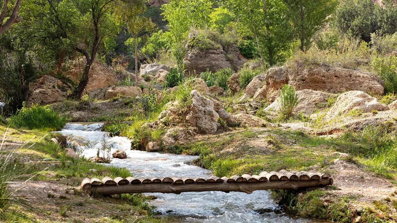 Un puente rústico cruza un arroyo en un paisaje rocoso y verde. Descubre cómo llegar a este rincón natural.