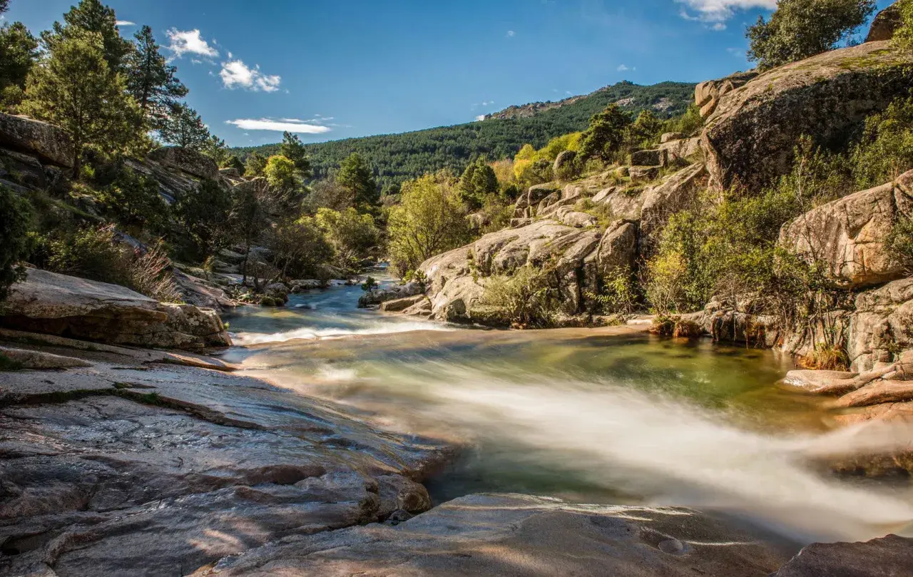 Un río serpentea entre rocas y vegetación, un paisaje idílico para descubrir rutas con encanto cerca de Madrid.
