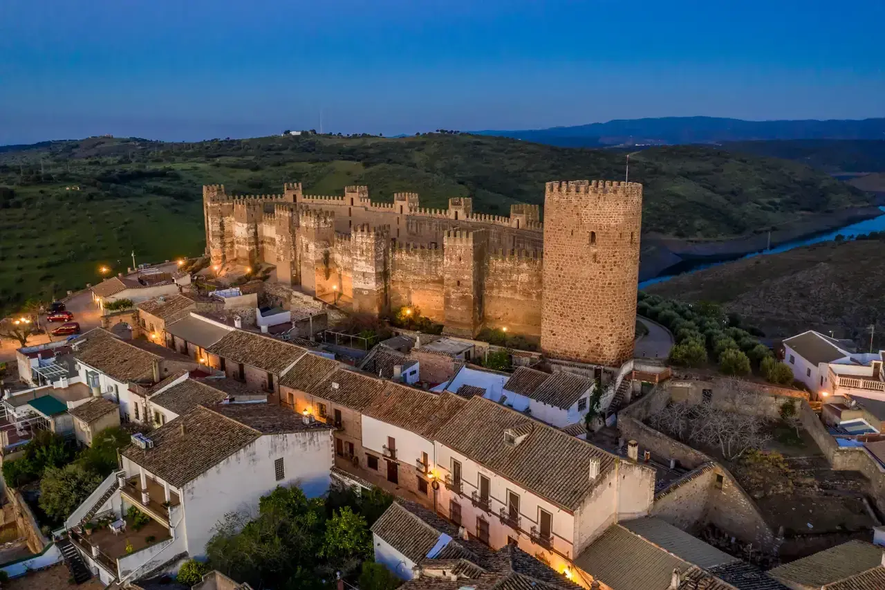 Imponente castillo, posiblemente el castillo más antiguo de España, iluminado al anochecer sobre un pueblo blanco.
