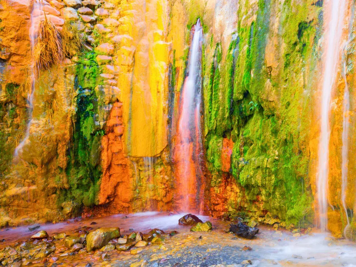 La cascada de los colores, un espectáculo natural con agua cayendo sobre rocas teñidas de vibrantes tonos ocres, verdes y amarillos.