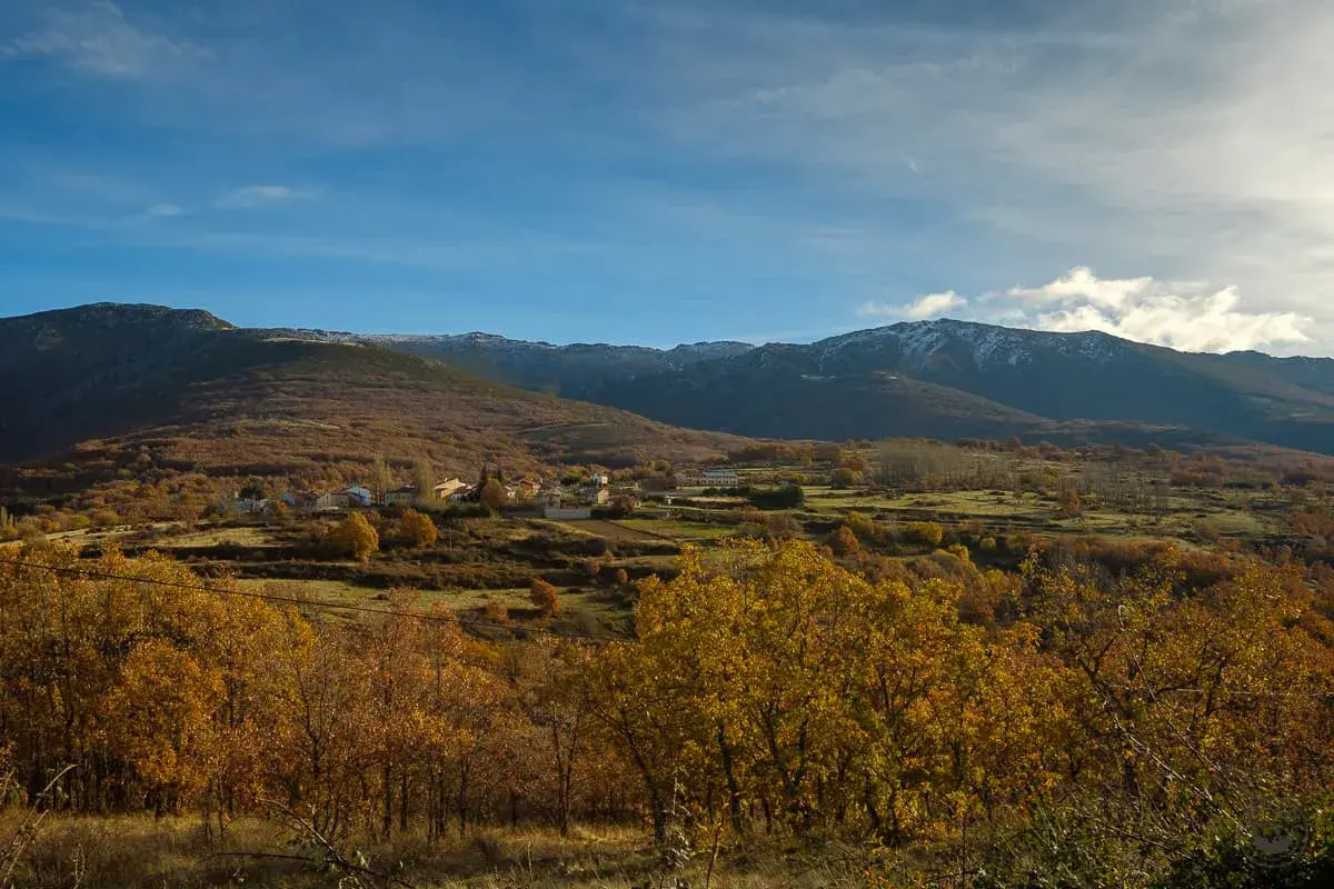 Paisaje otoñal con un pueblo en la ladera. Las montañas nevadas al fondo sugieren la ruta a la laguna negra.