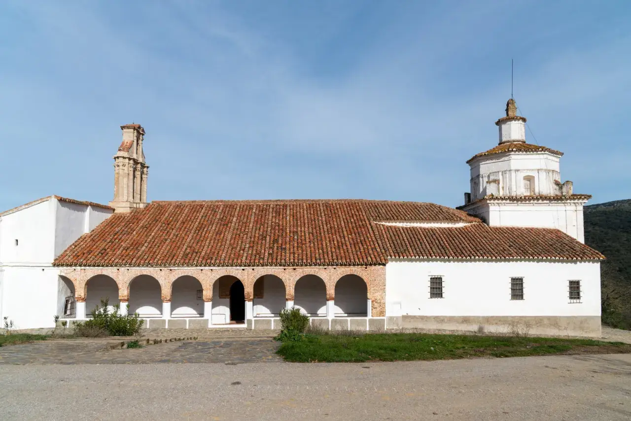 La ermita Virgen del Ara, con su tejado de tejas rojas y arcos blancos, se alza bajo un cielo azul.