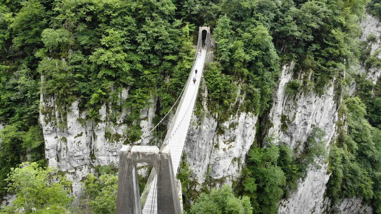La pasarela de Holtzarte cruza un profundo cañón verde, con personas caminando sobre ella.