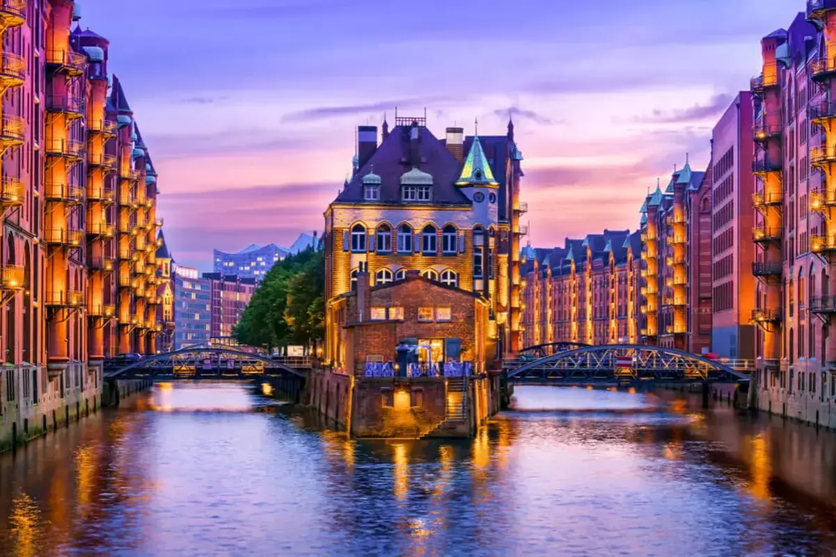 Canal de Hamburgo al atardecer, perfecto para saber donde ir en el puente de diciembre. Edificios de ladrillo iluminados reflejándose en el agua.