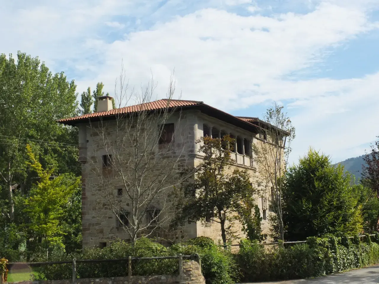 Edificio de piedra con tejado rojo y balcones, rodeado de árboles verdes. Un lugar con encanto, ideal para saber artziniega como llegar.