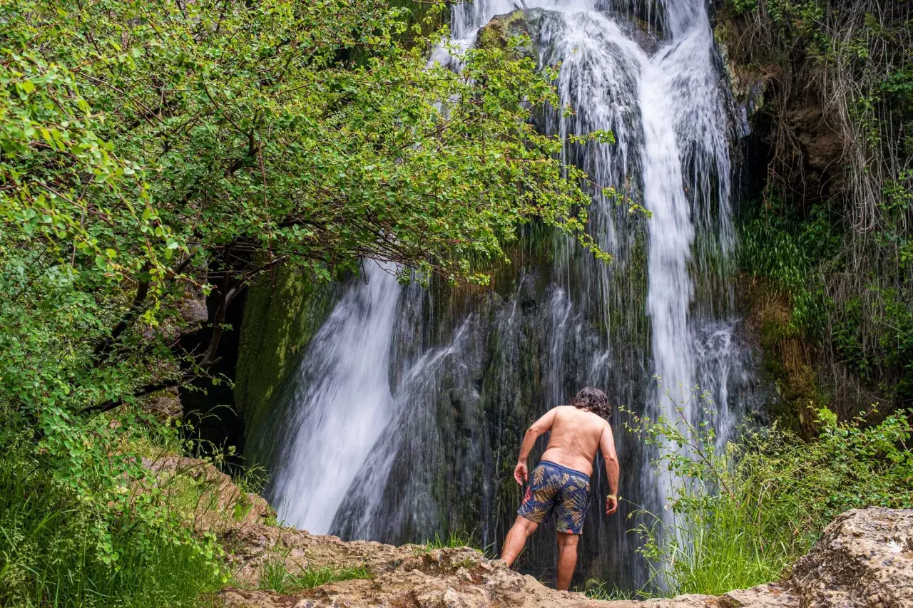 Hombre de espaldas admira la cascada en la ruta del barranco de la Hoz. Naturaleza exuberante y agua en movimiento.