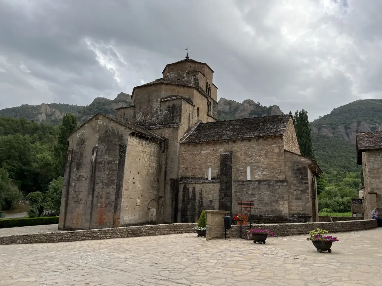 Iglesia románica de piedra con montañas al fondo. Un lugar histórico que evoca la grandeza del puente la reina.