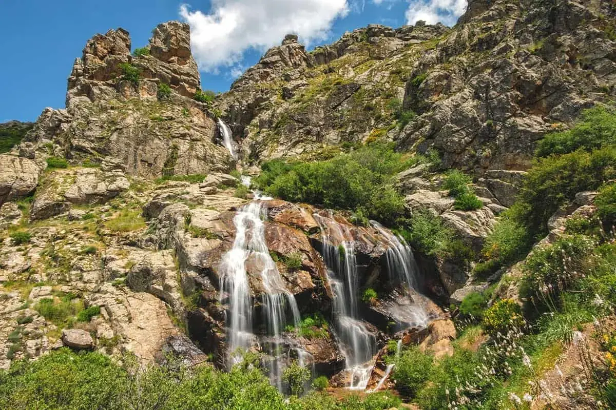 La cascada de los litueros desciende por rocas escarpadas, rodeada de vegetación exuberante bajo un cielo azul con nubes.