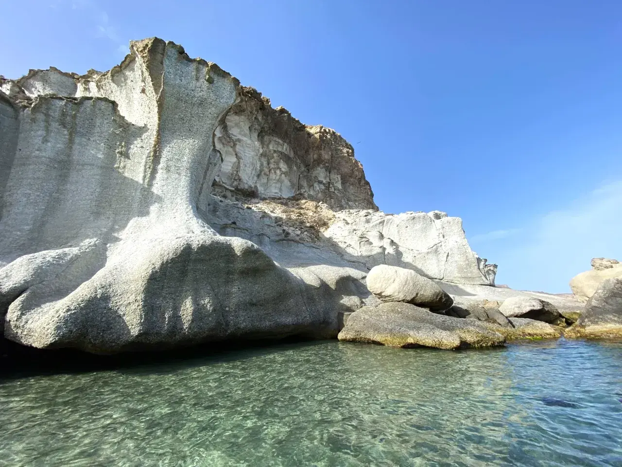 Aguas cristalinas bañan la base de imponentes rocas erosionadas en la cala de enmedio. El sol ilumina el paisaje, creando un contraste entre la piedra y el mar azul.