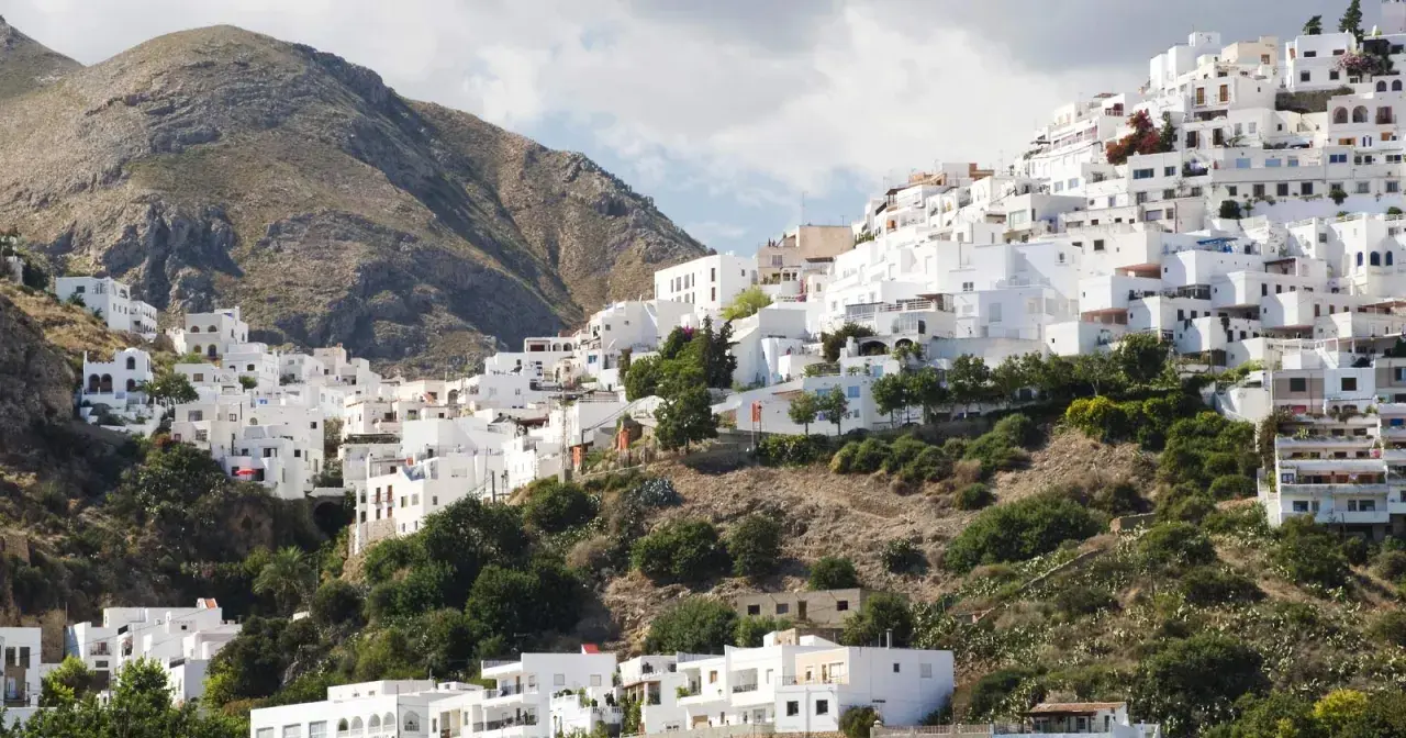 Casas blancas se aferran a una ladera montañosa, un laberinto de calles que invitan a descubrir Mojácar. ¿Cómo llegar? Sigue el sol.