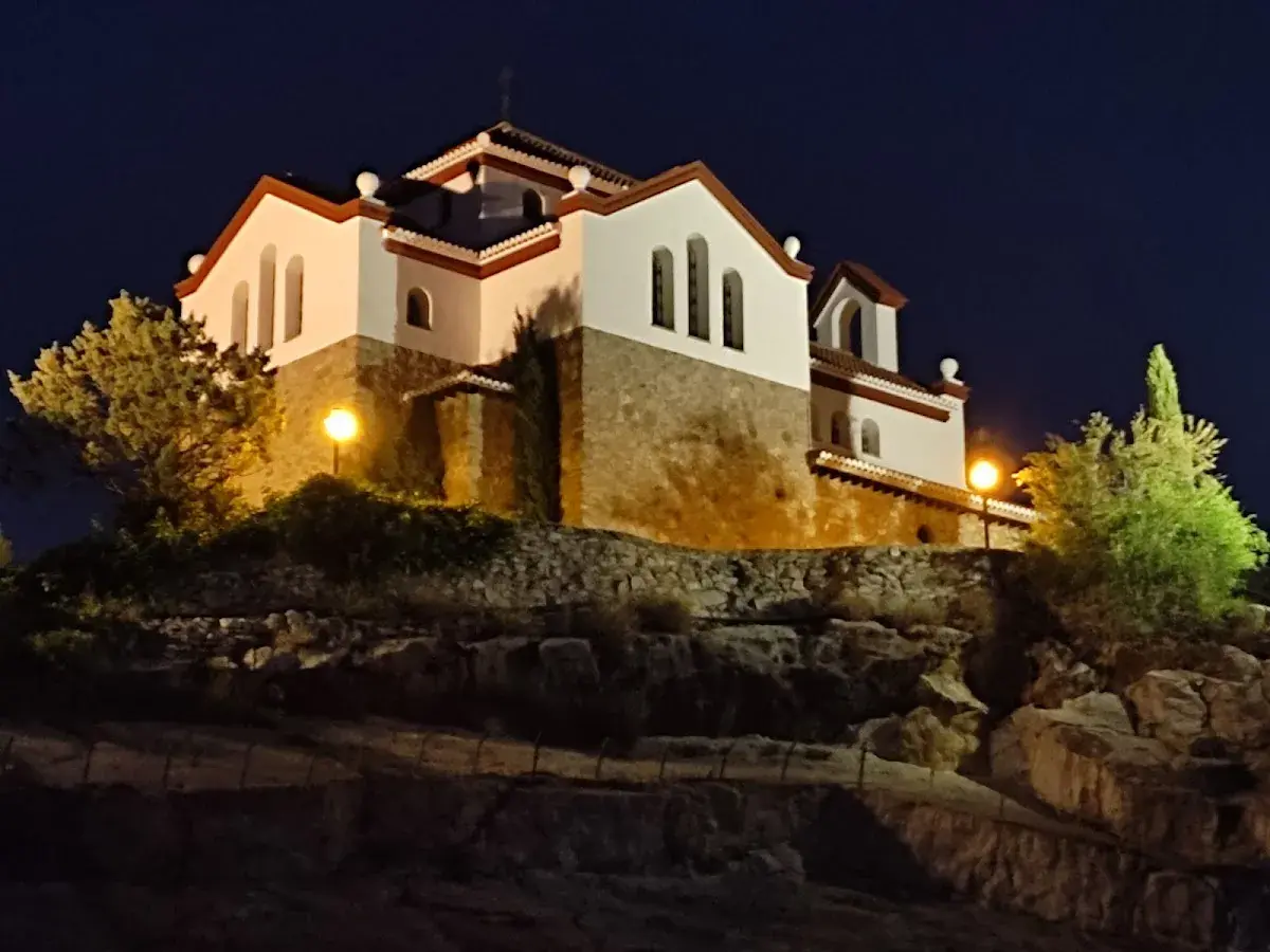 La ermita de los Tres Juanes, iluminada de noche, se alza sobre una colina rocosa.