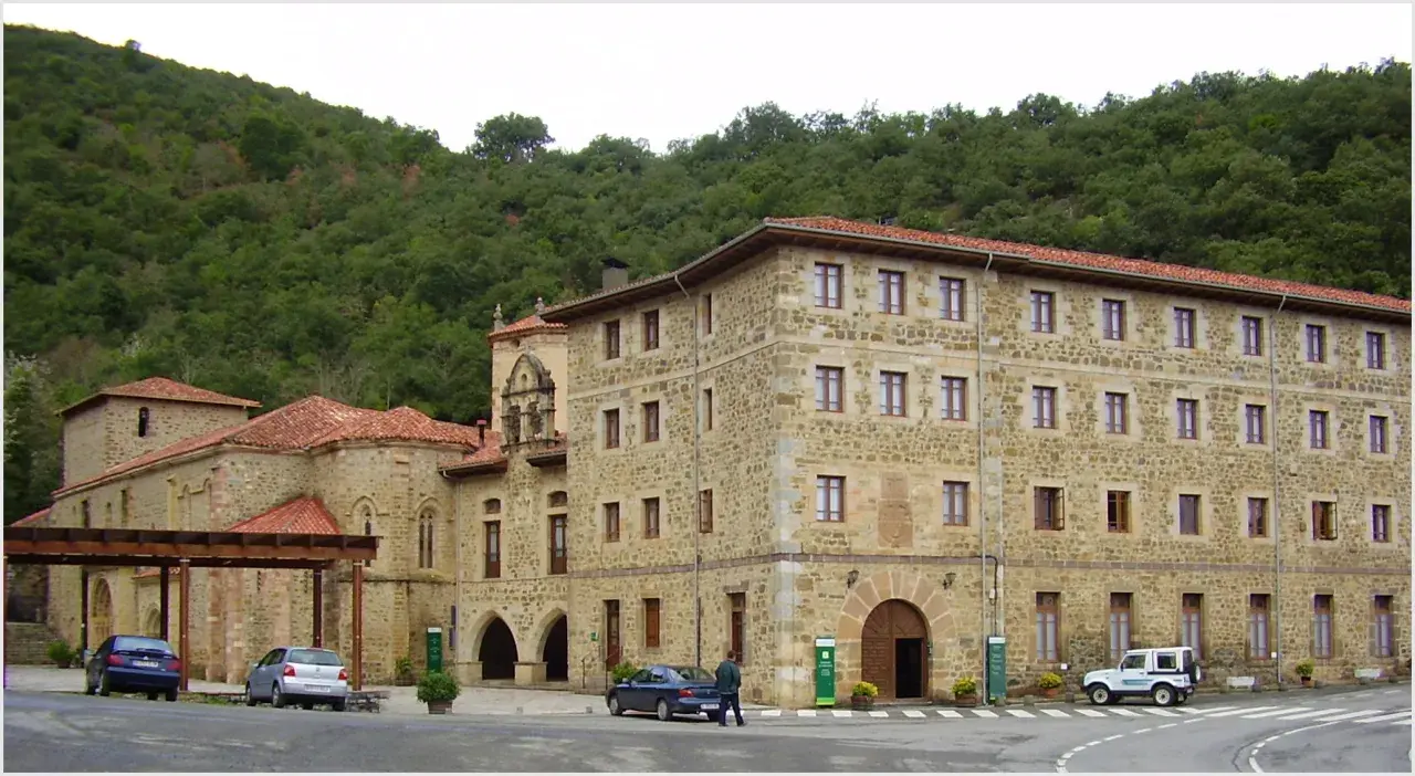 Edificio de piedra con tejados rojos, parte del monasterio de Santo Toribio de Liébana, rodeado de vegetación.
